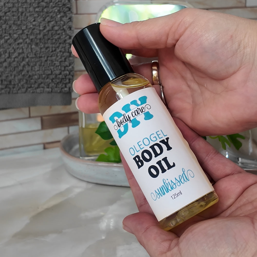 Two hands cup together holding a clear bottle with black lid. The bottle has a golden liquid inside and the bottle is labelled as Oleogel Body Oil.