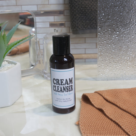 A brown bottle with black cap and white product label stands on a marble surface surrounded by bathroom accessories and plant.