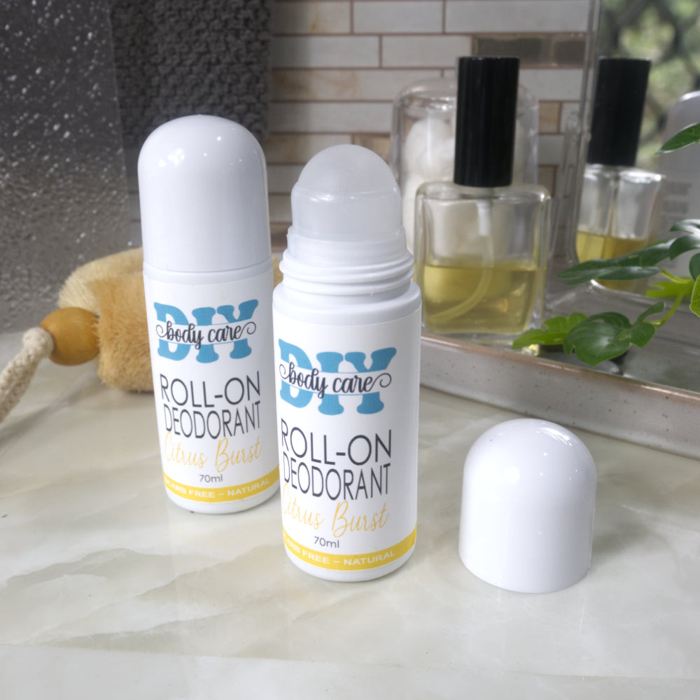 Two bottles of Roll-On deodorant stand upright on a bathroom counter top next to a stone tray with perfume and mirror. One bottle has a dome lid on while the second has the lid removed and placed to the right revealing a ball mechanism