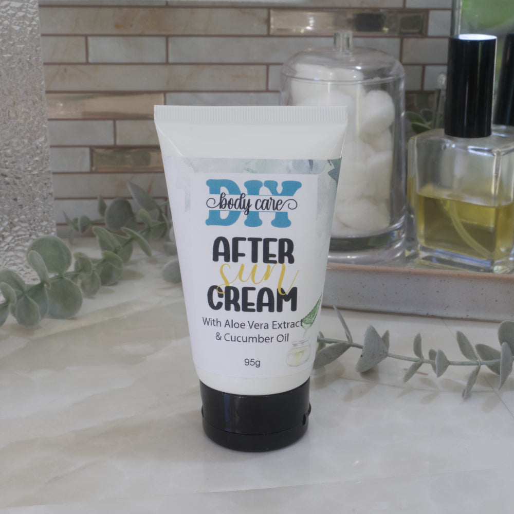 A white tube with black flip-top lid stands on a marble bathroom counter top with a bottle of perfume and jar of cotton balls behind.  The tube has a decorative label with the words AFTER SUN CREAM on it