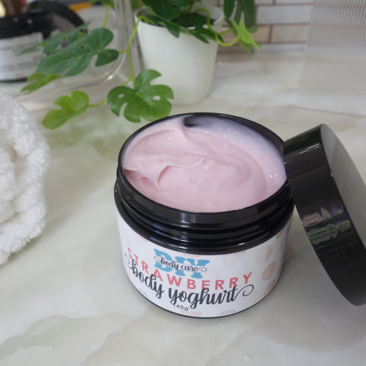 A black jar with a white and pink label sits on a marble counter surounded by a mirror, plant and towel.  The black lid has been removed and rests against the side of the jar revealing a pink cream.