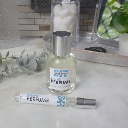 A small clear round bottle of perfume with a silver cap stands on a light marble surface.  Placed in front is a long narrow 10ml spray bottle. The label reads 'DIY Body Care Dry Oil Perfume'.