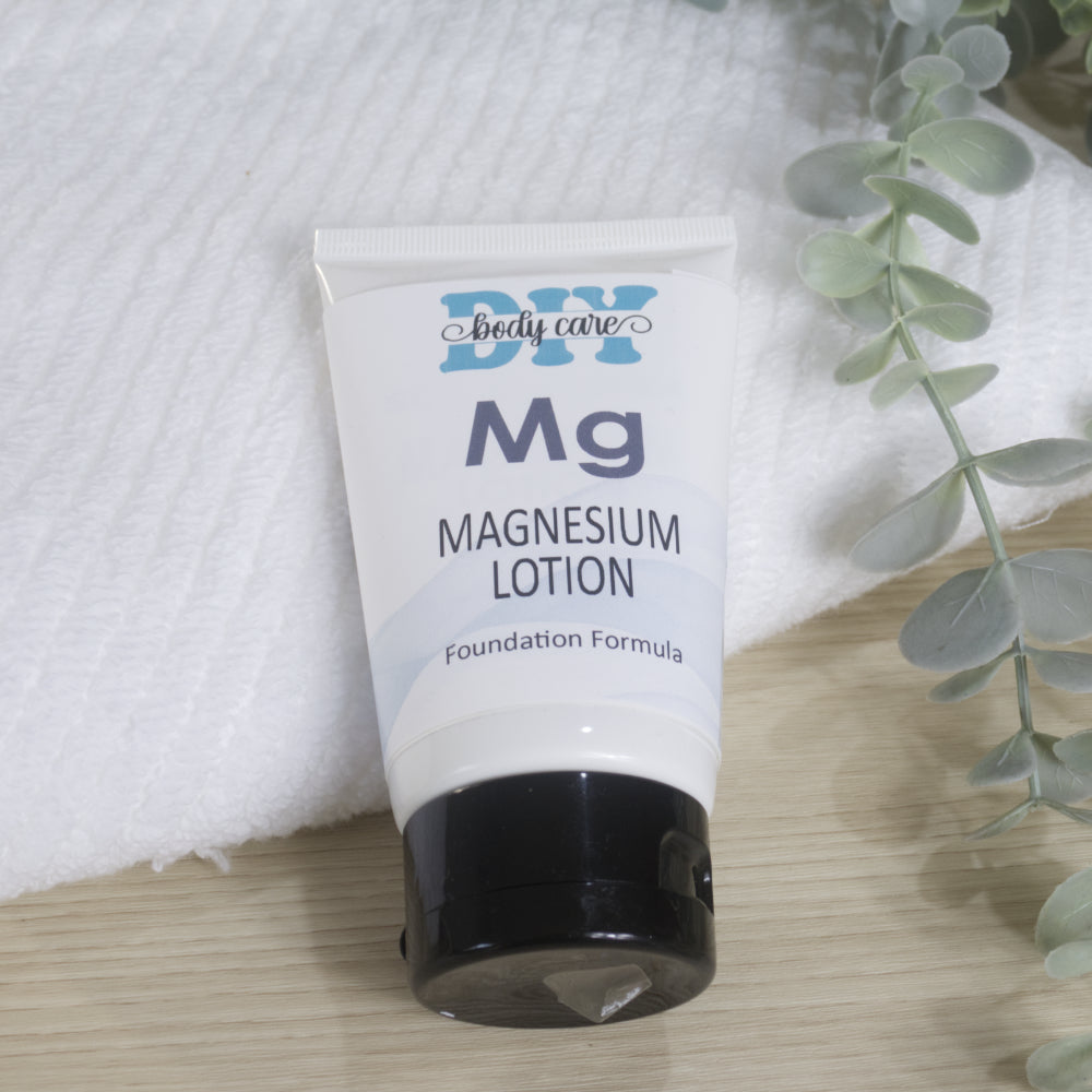 A white tube with black flip-top cap labelled as Magnesium lotion rests against a folder with towel with a piece of eucalptus