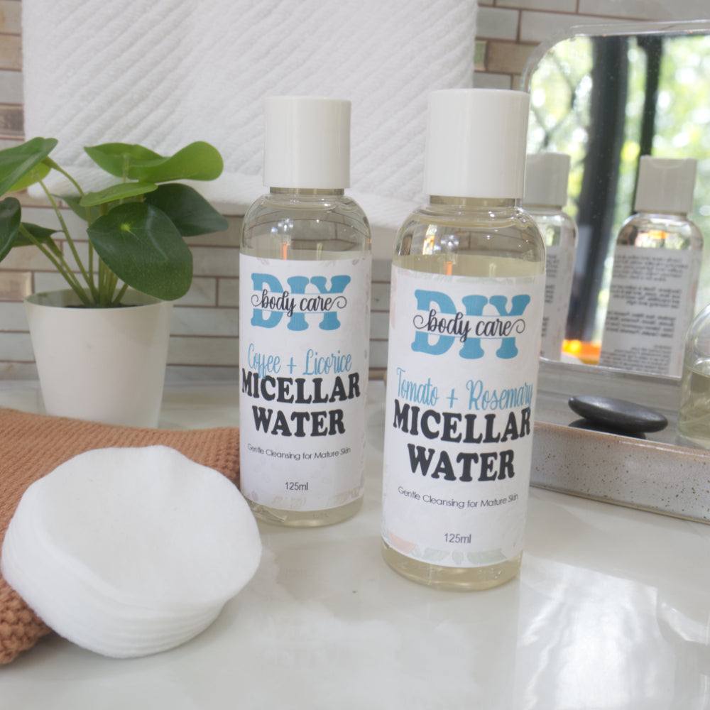 Two clear bottles with white caps and filled with clear liquid stang on a bathroom counter top along with a stack of cotton pads.  The bottles are labelled as Micellar Water but with slight ingredient variations.