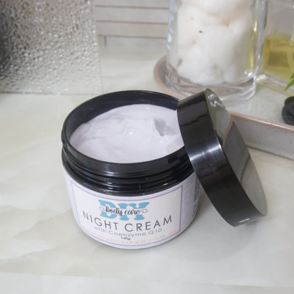 A black jar with a decorative purple label marked as NIGHT CREAM, sits on a bathroom counter top.  The lid has been removed and is resting on the side of the jar revealing a light purple cream inside.