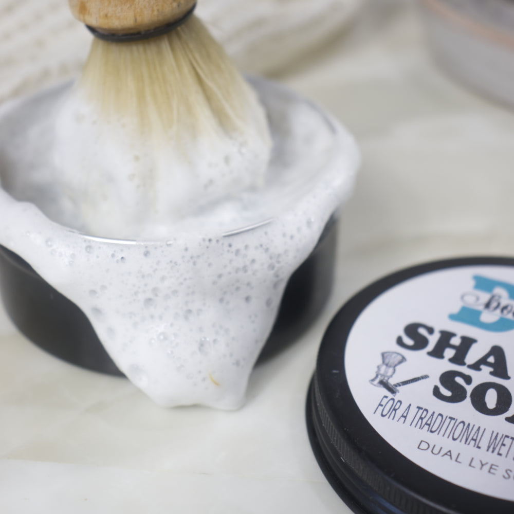A closs up image of a round black tin of shaving soap with a dense foam spilling over the edge