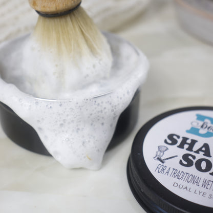 A closs up image of a round black tin of shaving soap with a dense foam spilling over the edge