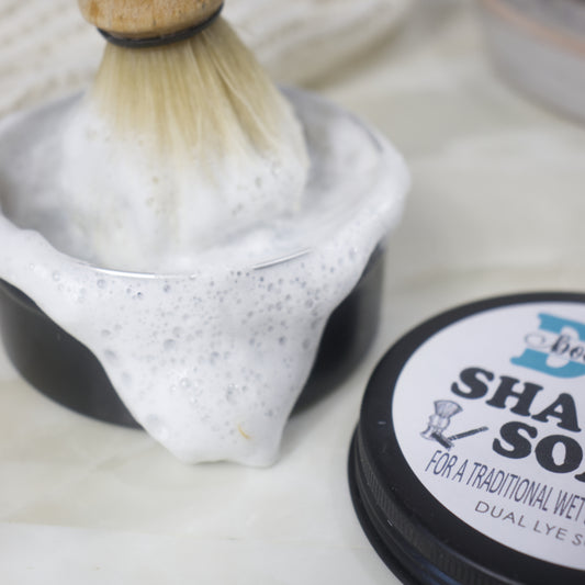 A closs up image of a round black tin of shaving soap with a dense foam spilling over the edge