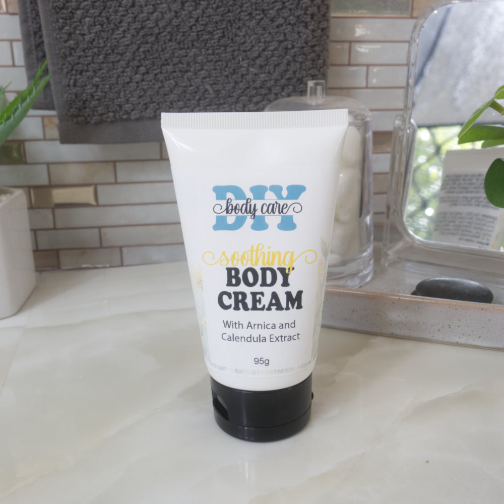 A white tube with black cap stands on a bathroom countertop and is labelled as Soothing Body Cream with arnica and calendula Extract.