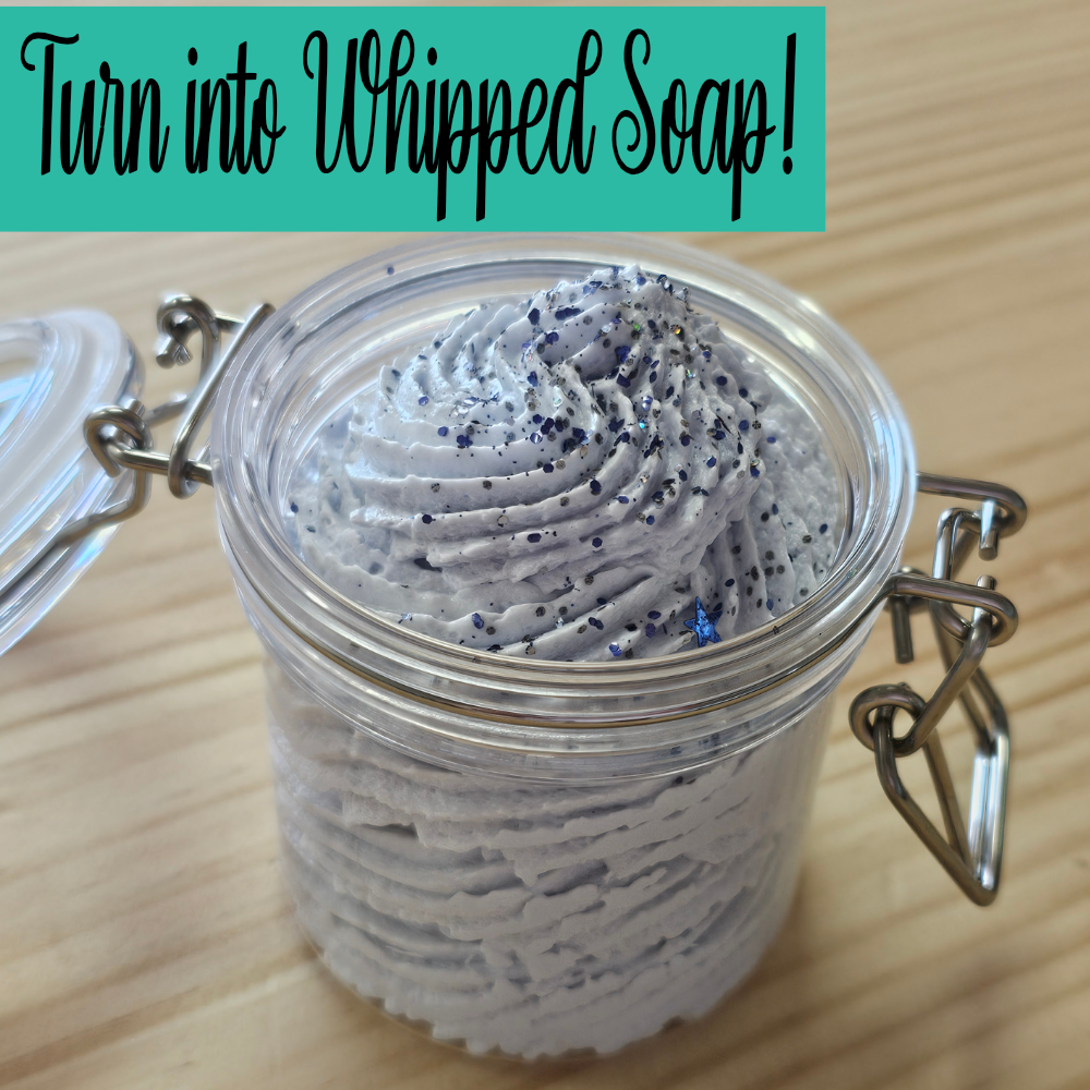 A clear jar with clip lock lids sits open on a wooden surface and is filled with a pale blue whipped soap with glitter on top.  Text overlay reads TURN INTO WHIPPED SOAP